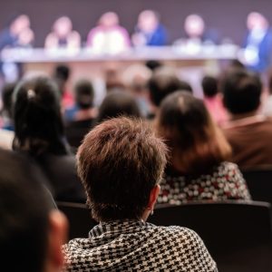 Rear view of Audience in the conference hall or seminar meeting which have Speakers are Brainstorming and talking on the stage, business and education about investment concept